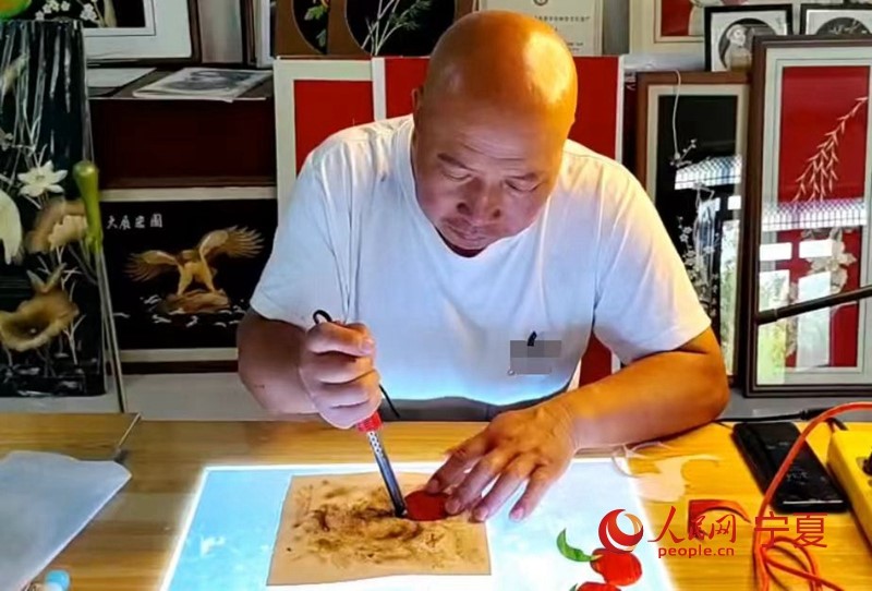 Weng Guosheng, un artesano de 54 a?os de la región autónoma Hui de Ningxia, en el noroeste de China, utiliza un soldador para planchar y colorear pajitas de trigo mientras crea una pintura con este material especial. (Diario del Pueblo digital/Li Tiantian)