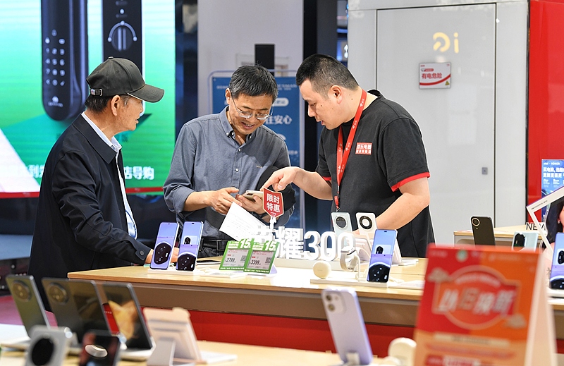 Consumidores se informan sobre los detalles de un teléfono móvil a la venta en un centro comercial de Shushan, Hefei, provincia de Anhui, 26 de abril del 2025. [Foto: VCG]