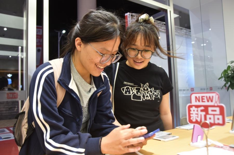 Dos jóvenes recién graduadas de la secundaria prueban teléfonos móviles en una tienda de la ciudad de Mengzi, en la provincia suroccidental china de Yunnan, el 24 de junio de 2025. (Xinhua/Xue Yingying)