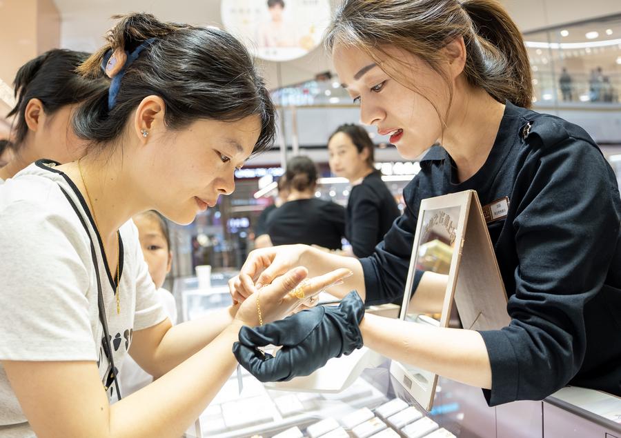 Una cliente (izq.) prueba joyas de oro en un centro comercial en la ciudad de Nantong, provincia de Jiangsu, este de China, el 3 de mayo de 2025. (Xinhua/Zhai Huiyong)