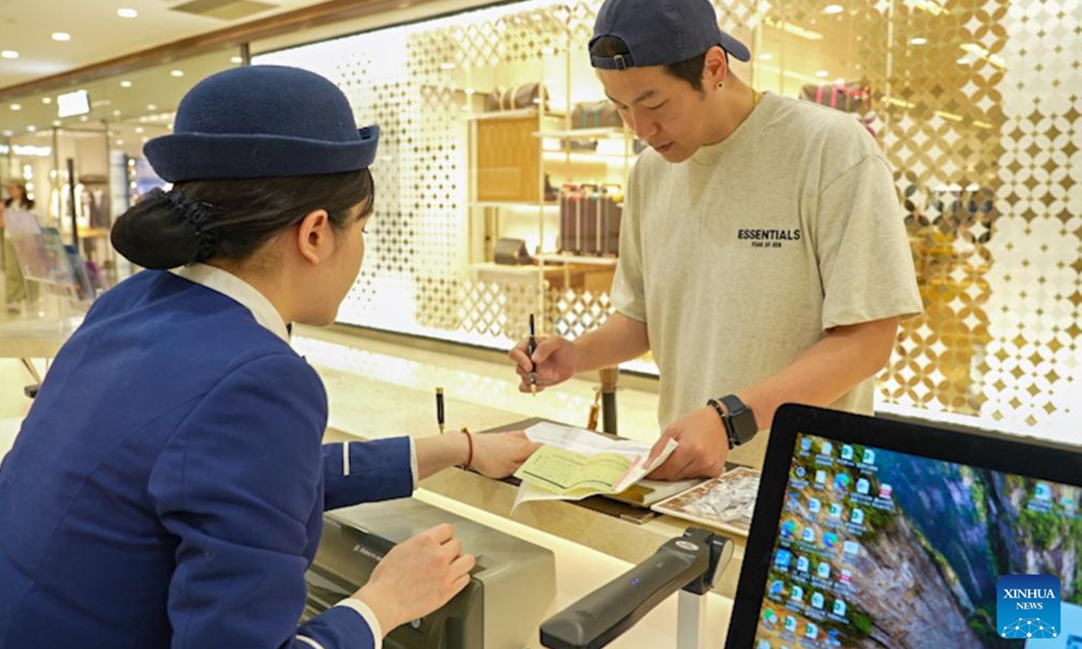 Un empleado (izq.) presta el servicio de reembolso de impuestos de salida a un turista surcoreano en un centro comercial de la municipalidad de Chongqing, suroeste de China, el 11 de abril de 2025. (Foto: Xinhua)